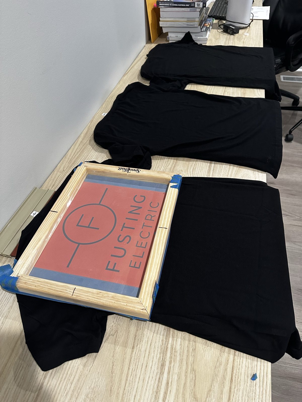 Fusting Electric logo screen positioned over black company T-shirts